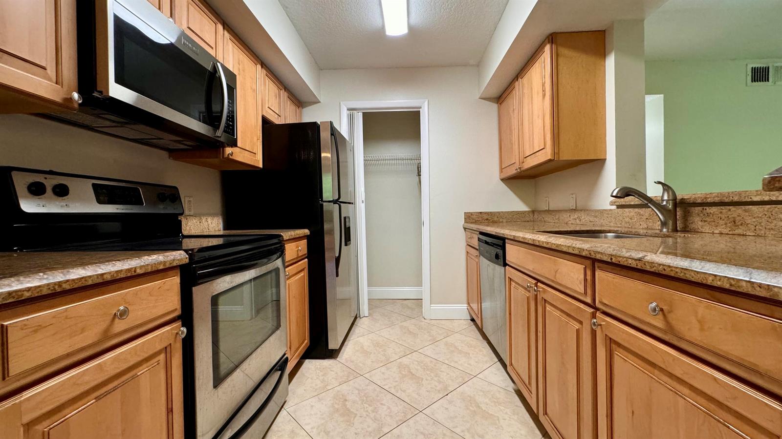 A galley kitchen features light wood cabinets, granite countertops, and stainless steel appliances — 815 W Boynton Beach Boulevard # 105, Boynton Beach FL 33426, BOYNTON BEACH, FL