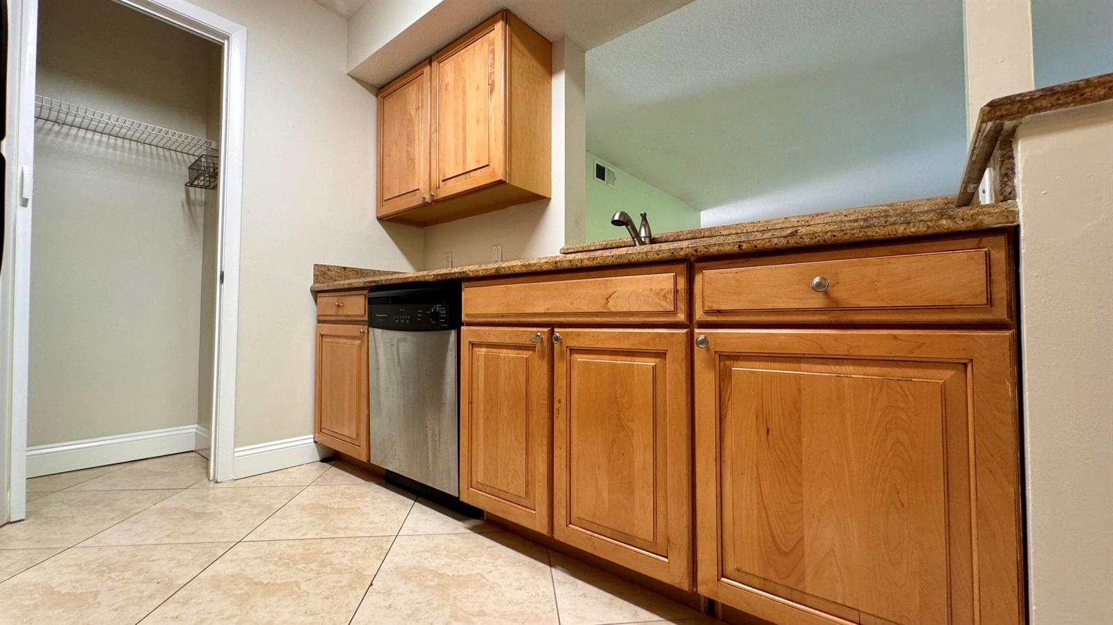 A kitchen features wood cabinets, granite countertops, a stainless steel dishwasher, and tiled flooring — 815 W Boynton Beach Boulevard # 105, Boynton Beach FL 33426, BOYNTON BEACH, FL