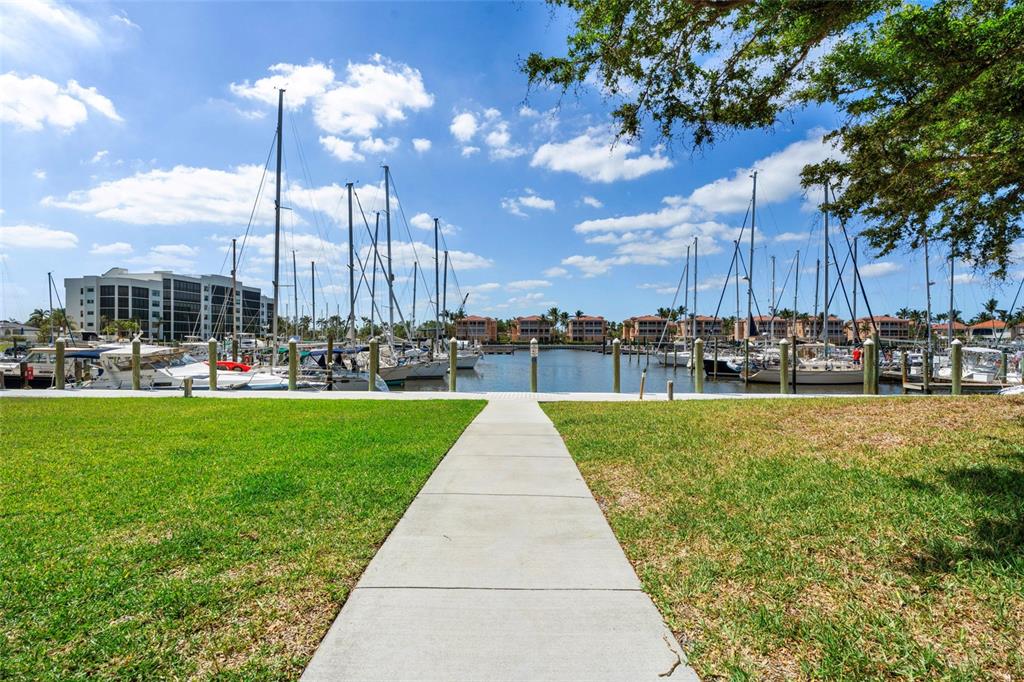 A concrete walkway leads through a grassy lawn toward a marina filled with docked sailboats — 2060 MATECUMBE KEY ROAD UNIT 2106, PUNTA GORDA, FL