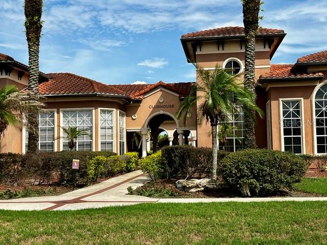 A tan clubhouse building features a central arched entrance, tiled roof, and surrounding palm trees — 5554 METROWEST BOULEVARD UNIT 212, ORLANDO, FL