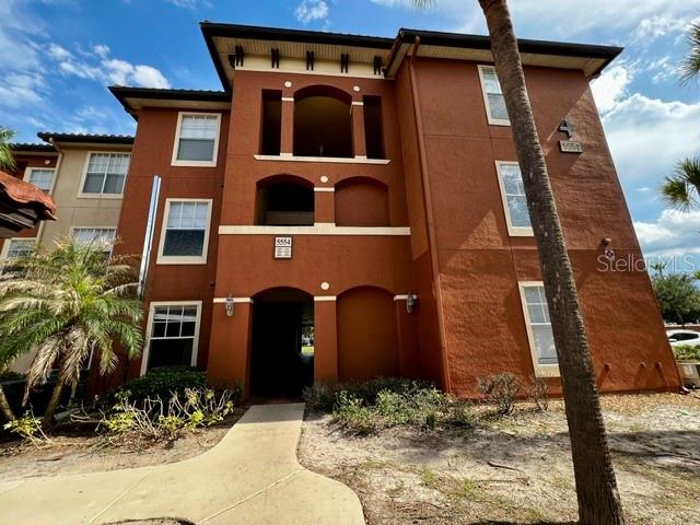A multi-story apartment building with a terracotta-colored stucco exterior and a palm tree — 5554 METROWEST BOULEVARD UNIT 212, ORLANDO, FL