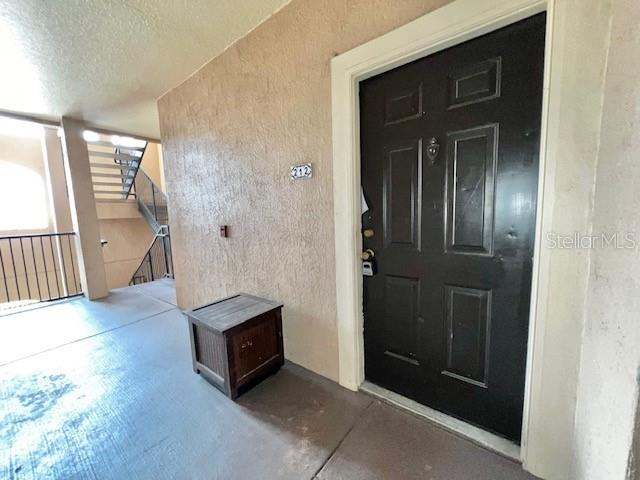 A dark brown front door with a small wooden storage chest sits on a concrete walkway — 5554 METROWEST BOULEVARD UNIT 212, ORLANDO, FL
