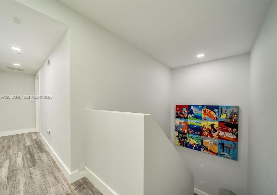 A hallway with wood-look flooring leads to a staircase featuring a colorful multi-panel wall art — 140 S Dixie Hwy, Hollywood FL 33020, HOLLYWOOD, FL