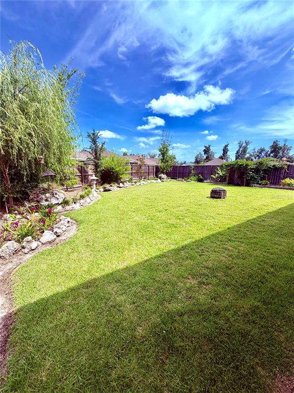 A grassy backyard features a stone-bordered garden bed, a weeping willow, and a wooden fence — 1464 SW 66TH WAY, GAINESVILLE, FL