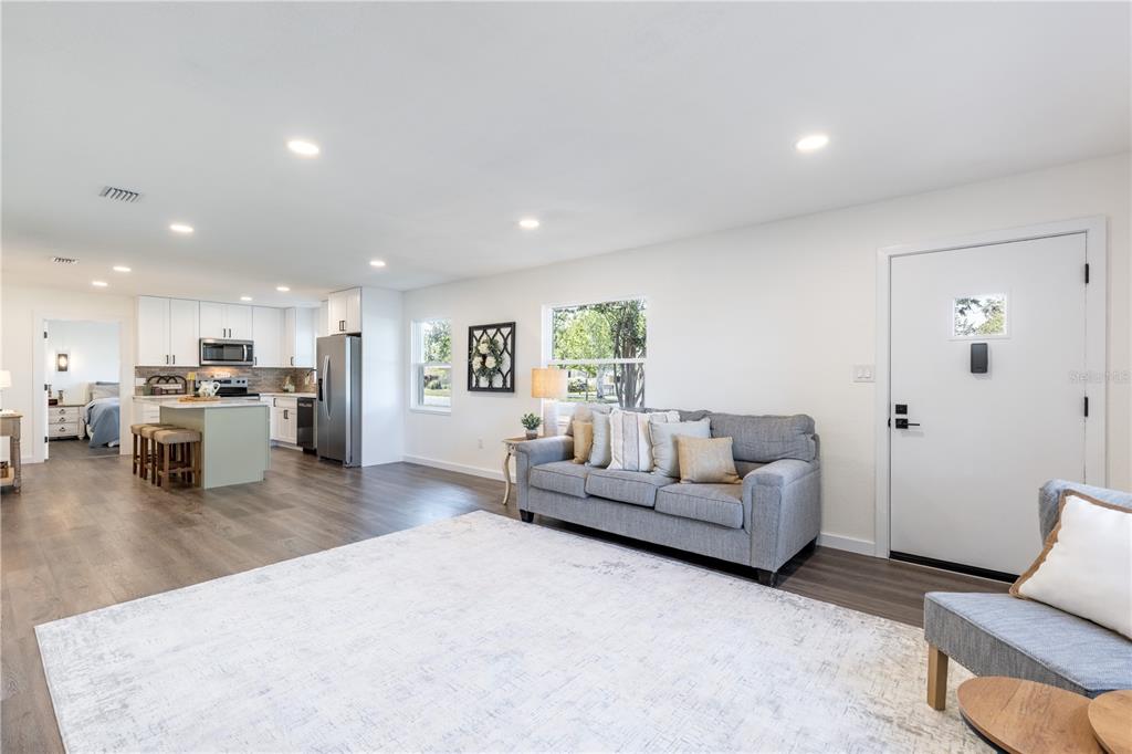 An open-concept living room and kitchen feature white cabinetry, gray flooring, and a gray sofa — 1201 SHERMAN AVENUE, TAVARES, FL