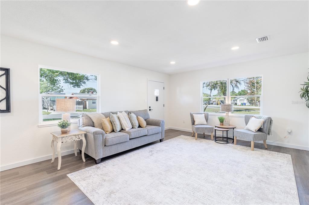 A living room with gray flooring, a gray sofa, two armchairs, and a large rug — 1201 SHERMAN AVENUE, TAVARES, FL