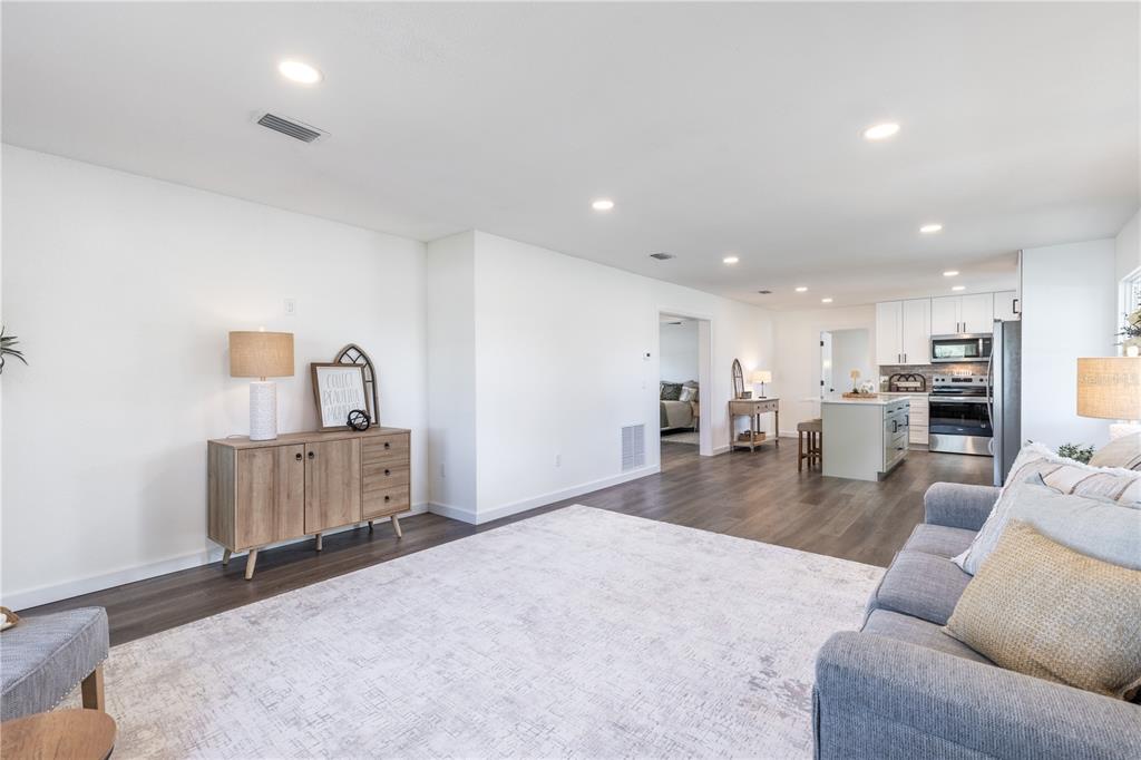 An open-concept living room features wood-look flooring, a light-colored area rug, and a kitchen beyond — 1201 SHERMAN AVENUE, TAVARES, FL