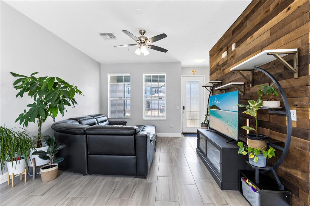 A living room features a black sectional sofa, a wood-paneled accent wall, and tile flooring — 6187 CHAPLEDALE DRIVE, ORLANDO, FL