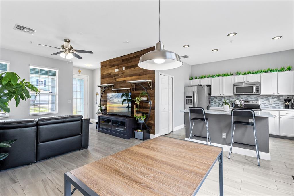 An open-concept living room and kitchen feature wood-plank accent walls and gray tile flooring — 6187 CHAPLEDALE DRIVE, ORLANDO, FL