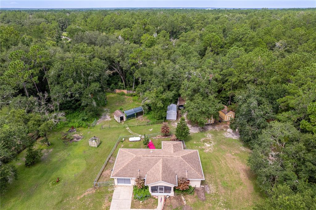 An aerial view shows a single-story house with a brown roof surrounded by wooded land — 3063 CRUM ROAD, BROOKSVILLE, FL