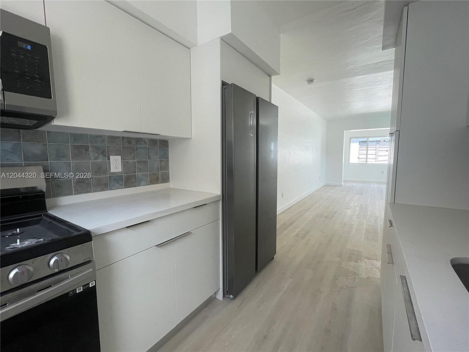 A kitchen with white cabinets, stainless steel appliances, and light wood flooring leads to a hallway — 2120 Biarritz Dr # 1, Miami Beach FL 33141, MIAMI BEACH, FL