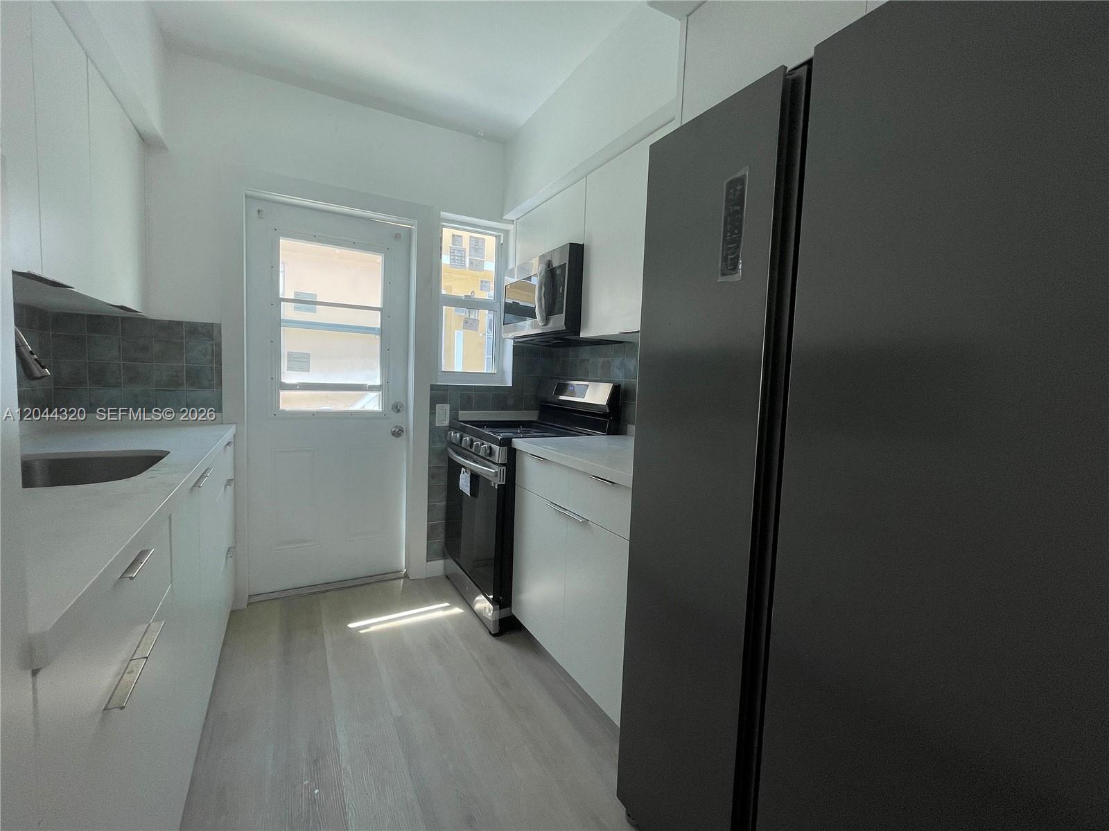 A galley-style kitchen features white cabinets, stainless steel appliances, and a glass-paneled exterior door — 2120 Biarritz Dr # 1, Miami Beach FL 33141, MIAMI BEACH, FL