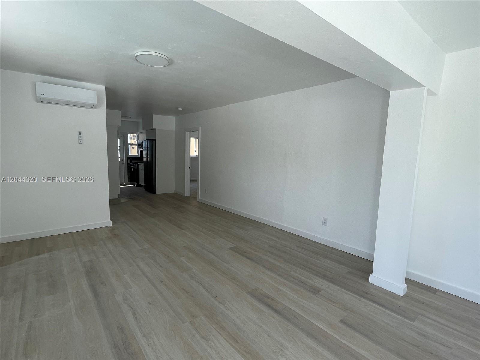 An empty room features white walls, light wood-look flooring, and a wall-mounted air conditioning unit — 2120 Biarritz Dr # 1, Miami Beach FL 33141, MIAMI BEACH, FL