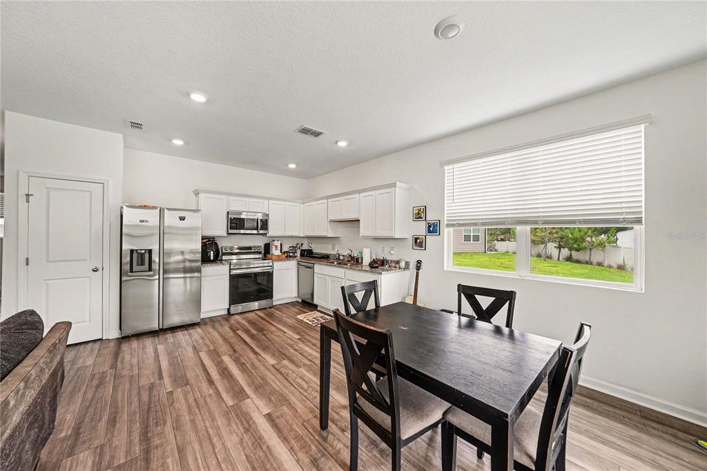 A kitchen and dining area with white cabinets, stainless steel appliances, and wood-look flooring — 6272 BUCKET COURT, GIBSONTON, FL