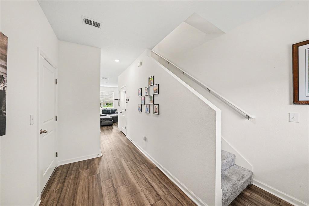 A hallway with wood-look flooring leads to a living area past a carpeted staircase — 6272 BUCKET COURT, GIBSONTON, FL