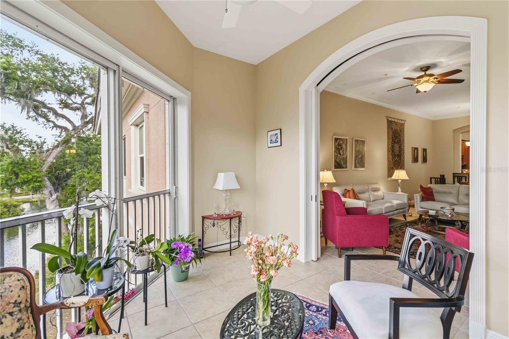 A sunroom with tile floors and a balcony overlooks a lake, opening into a living room — 5246 MANORWOOD DRIVE UNIT 4C, SARASOTA, FL