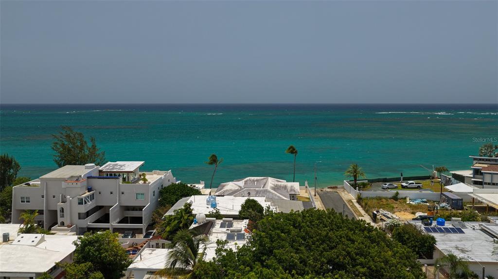 An aerial view shows a coastal neighborhood with white buildings, palm trees, and the ocean — 111 CALLE DONCELLA UNIT TH2, SAN JUAN, PR
