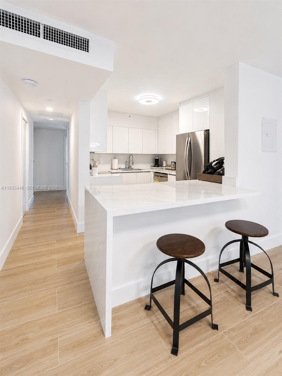 A modern kitchen with white cabinetry and a dining area featuring a glass table — 1500 Bay Rd # 724S, Miami Beach FL 33139, MIAMI BEACH, FL