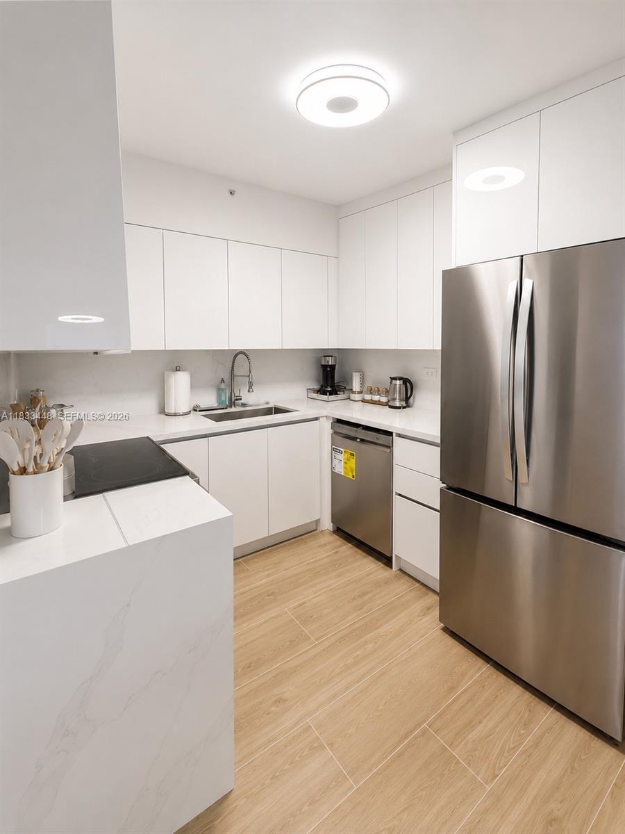 A modern kitchen features white cabinetry, stainless steel appliances, and light wood-look tile flooring — 1500 Bay Rd # 724S, Miami Beach FL 33139, MIAMI BEACH, FL