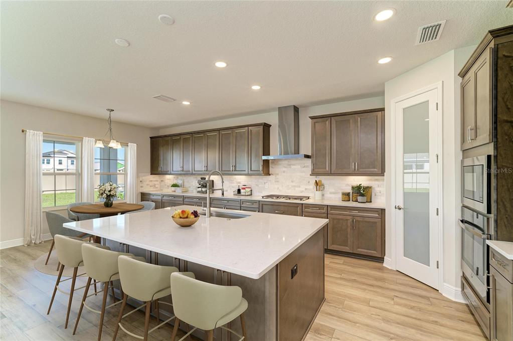 A modern kitchen features a large white island, gray cabinetry, stainless steel appliances, and wood flooring — 33882 TWILIGHT SEA PLACE, DADE CITY, FL