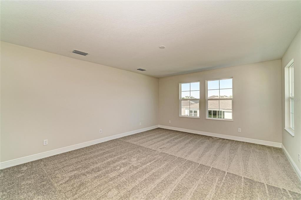 An empty room with beige walls, gray carpeting, and two windows overlooking a neighborhood — 33882 TWILIGHT SEA PLACE, DADE CITY, FL