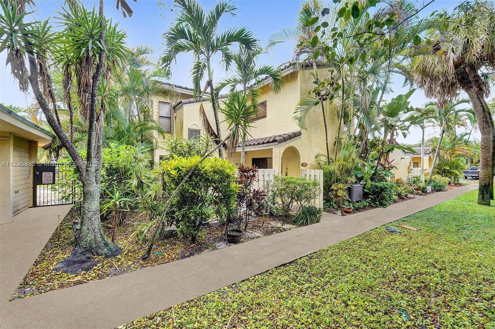 A two-story yellow stucco townhouse exterior surrounded by lush tropical landscaping and palm trees — 22322 Pineapple Walk Drive, Boca Raton FL 33433, BOCA RATON, FL