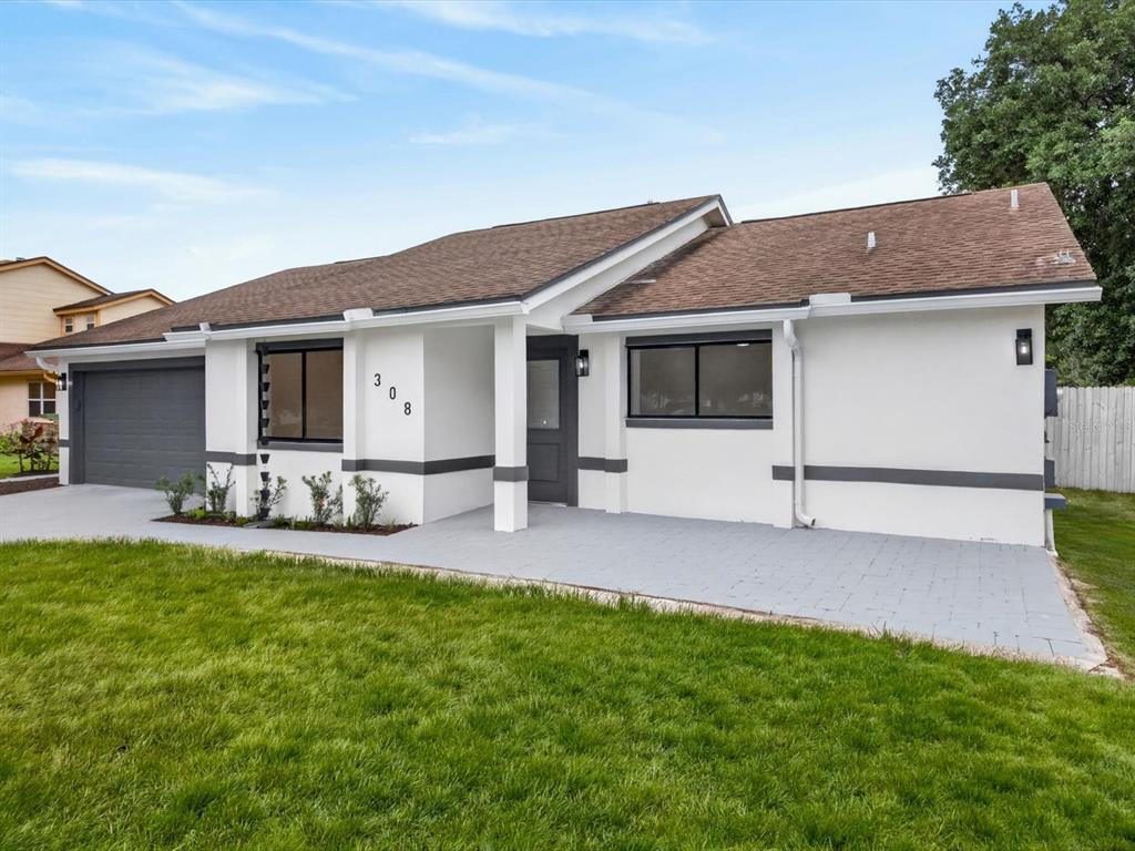 A single-story house with white stucco walls, gray trim, a brown roof, and a paved patio — 308 S SHADOW BAY DRIVE, ORLANDO, FL