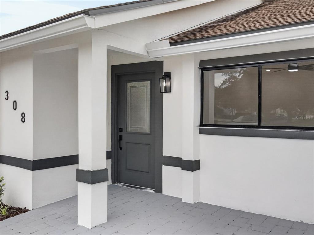 A white house exterior features a dark gray front door, matching trim, and paved porch — 308 S SHADOW BAY DRIVE, ORLANDO, FL