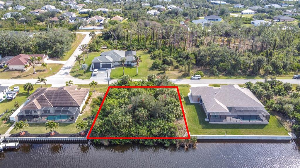 An aerial view shows a vacant, wooded waterfront lot situated between two residential homes — 9177 SANTA LUCIA DRIVE, PORT CHARLOTTE, FL