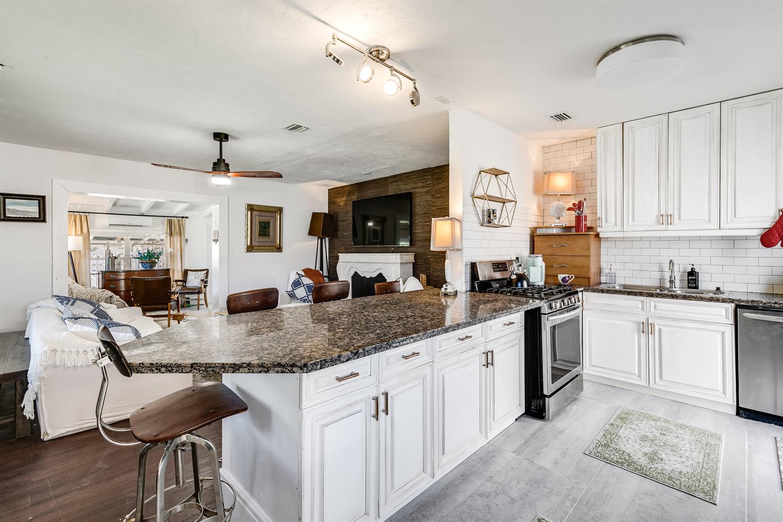 A kitchen with white cabinets and granite countertops overlooks a living area with a fireplace — 609 S Arnold Avenue, Lantana FL 33462, LANTANA, FL