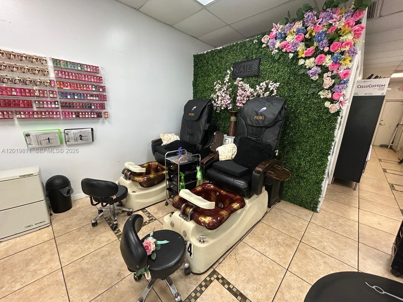 A nail salon features two pedicure chairs, a floral accent wall, and wall-mounted polish racks — 6630 Stirling Rd, Davie FL 33024, DAVIE, FL