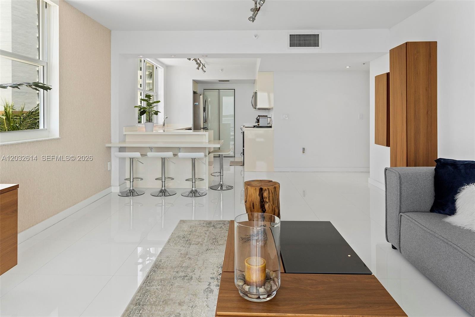 A modern living room features white tile floors, a breakfast bar, and a gray sofa — 800 CLAUGHTON ISLAND DRIVE # 505, Miami FL 33131, MIAMI, FL