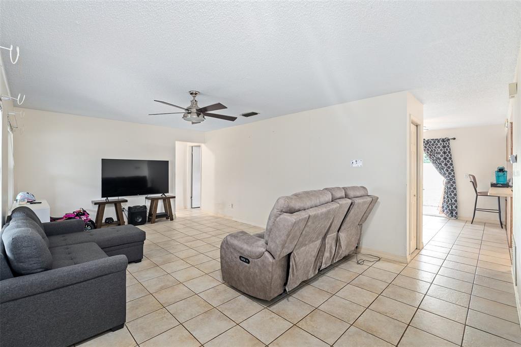 A living room features a grey sectional sofa, a large television, and tile flooring — 1218 MELLISA DRIVE, PORT ORANGE, FL