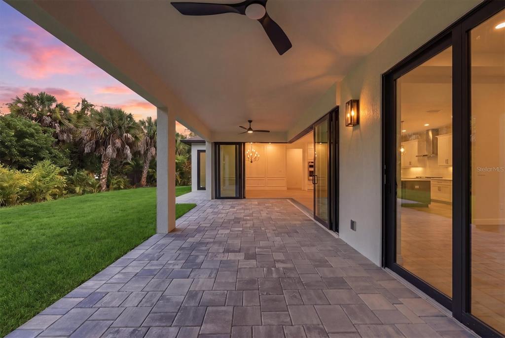 A covered outdoor patio with stone pavers overlooks a grassy lawn and palm trees — 166 MEDALIST ROAD, ROTONDA WEST, FL