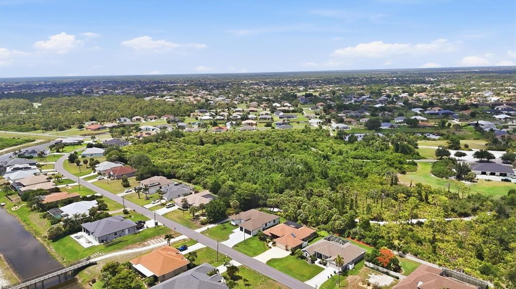An aerial view shows a residential neighborhood with houses surrounding a large, wooded vacant lot — 166 MEDALIST ROAD, ROTONDA WEST, FL