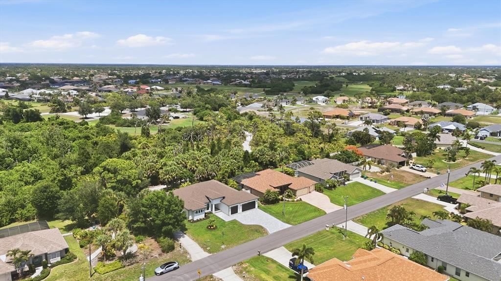An aerial view shows a suburban neighborhood with single-family homes, lush green trees, and streets — 166 MEDALIST ROAD, ROTONDA WEST, FL