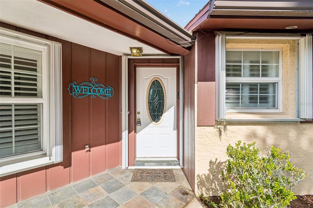 A front entryway features a white door with an oval glass insert and tile flooring — 7635 TANGLEWOOD DRIVE, NEW PORT RICHEY, FL