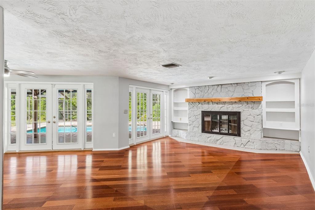 A living room features hardwood floors, a white stone fireplace, and glass doors to a pool — 7635 TANGLEWOOD DRIVE, NEW PORT RICHEY, FL