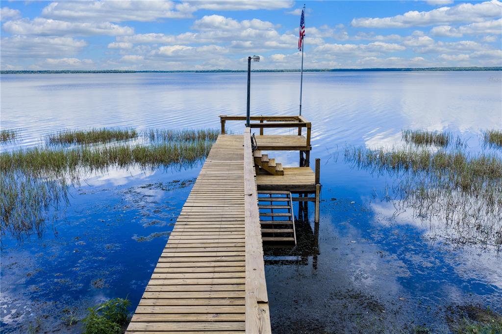 A wooden dock extends into a calm lake with grassy patches under a cloudy sky — 14014 SE 201ST TERRACE, HAWTHORNE, FL
