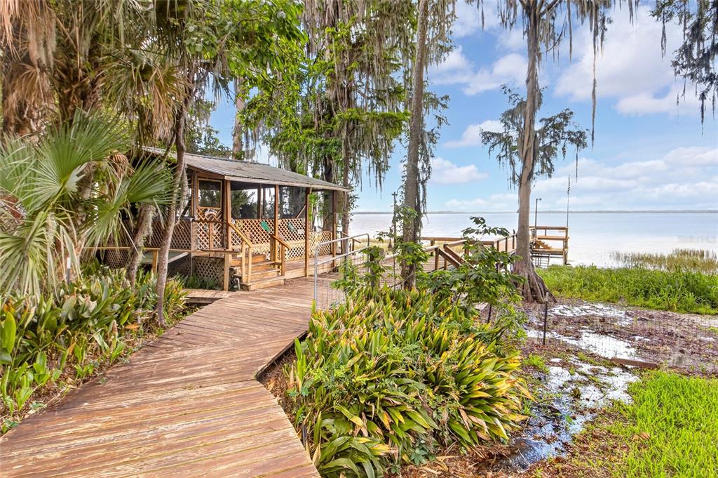 A wooden boardwalk leads to a screened-in cabin situated along a lake with a dock — 14014 SE 201ST TERRACE, HAWTHORNE, FL