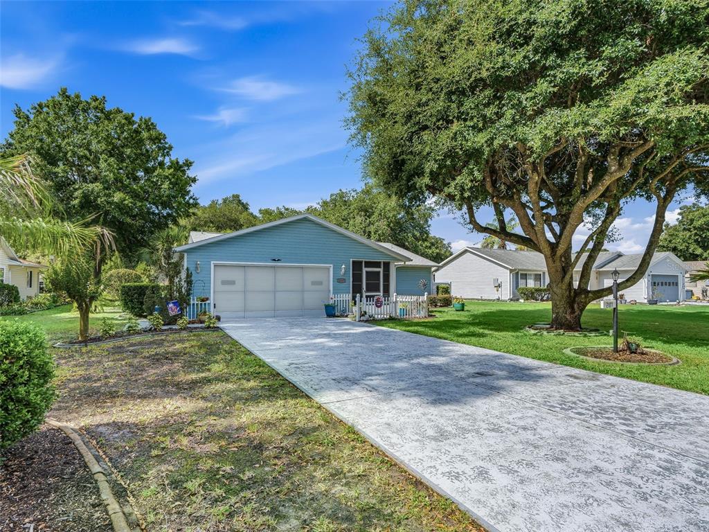 A light blue single-story house features a white garage door and a concrete driveway — 2107 GREENLAW COURT, LEESBURG, FL
