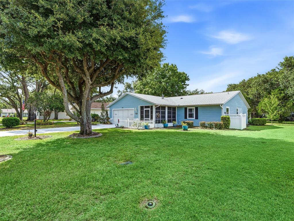 A single-story blue house with a large tree in the front yard — 2107 GREENLAW COURT, LEESBURG, FL