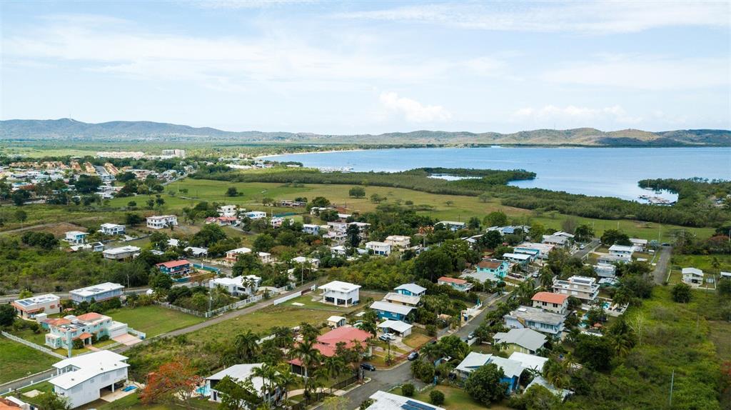 An aerial view shows a coastal neighborhood with houses, green vegetation, and a large bay — ST 307 KM 7.4, BOQUERON, PR
