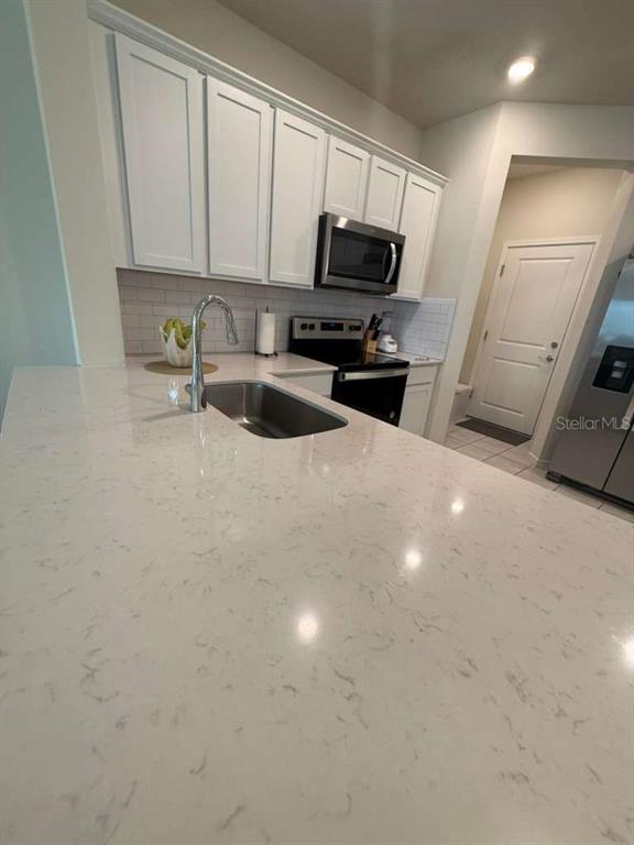 A kitchen features white cabinets, quartz countertops, a stainless steel sink, and stainless steel appliances — 2579 WINSOME WAY, DAVENPORT, FL