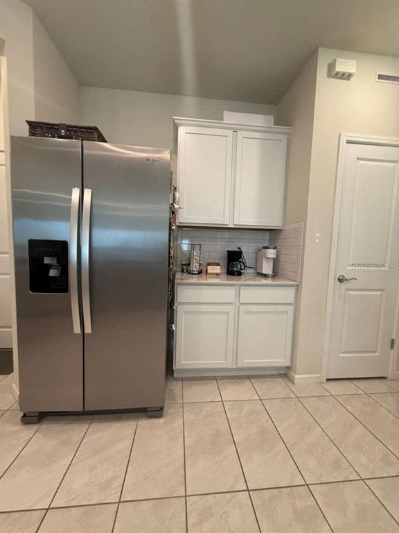 A kitchen features a stainless steel refrigerator, white cabinets, and light-colored tile flooring — 2579 WINSOME WAY, DAVENPORT, FL