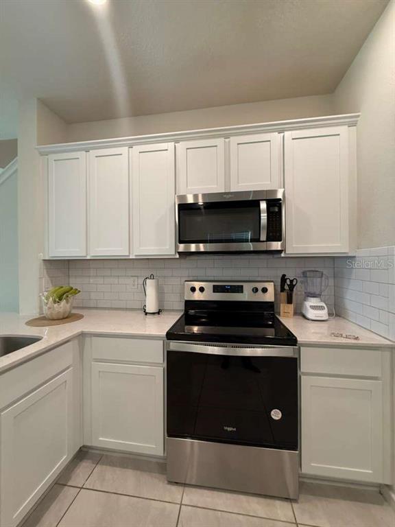 A kitchen features white cabinets, a stainless steel microwave and stove, and a subway tile backsplash — 2579 WINSOME WAY, DAVENPORT, FL
