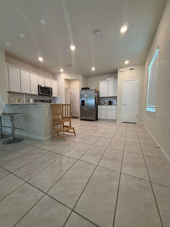 A kitchen features white cabinets, stainless steel appliances, a breakfast bar, and light tile flooring — 2579 WINSOME WAY, DAVENPORT, FL