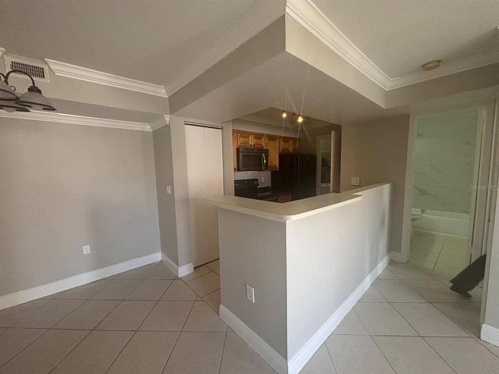 A kitchen with wood cabinets and a breakfast bar opens to a tiled dining area — 3038 PARKWAY BOULEVARD UNIT 208, KISSIMMEE, FL