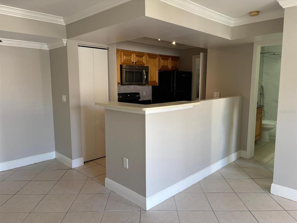 A kitchen with wood cabinets and black appliances overlooks a tiled living area — 3038 PARKWAY BOULEVARD UNIT 208, KISSIMMEE, FL