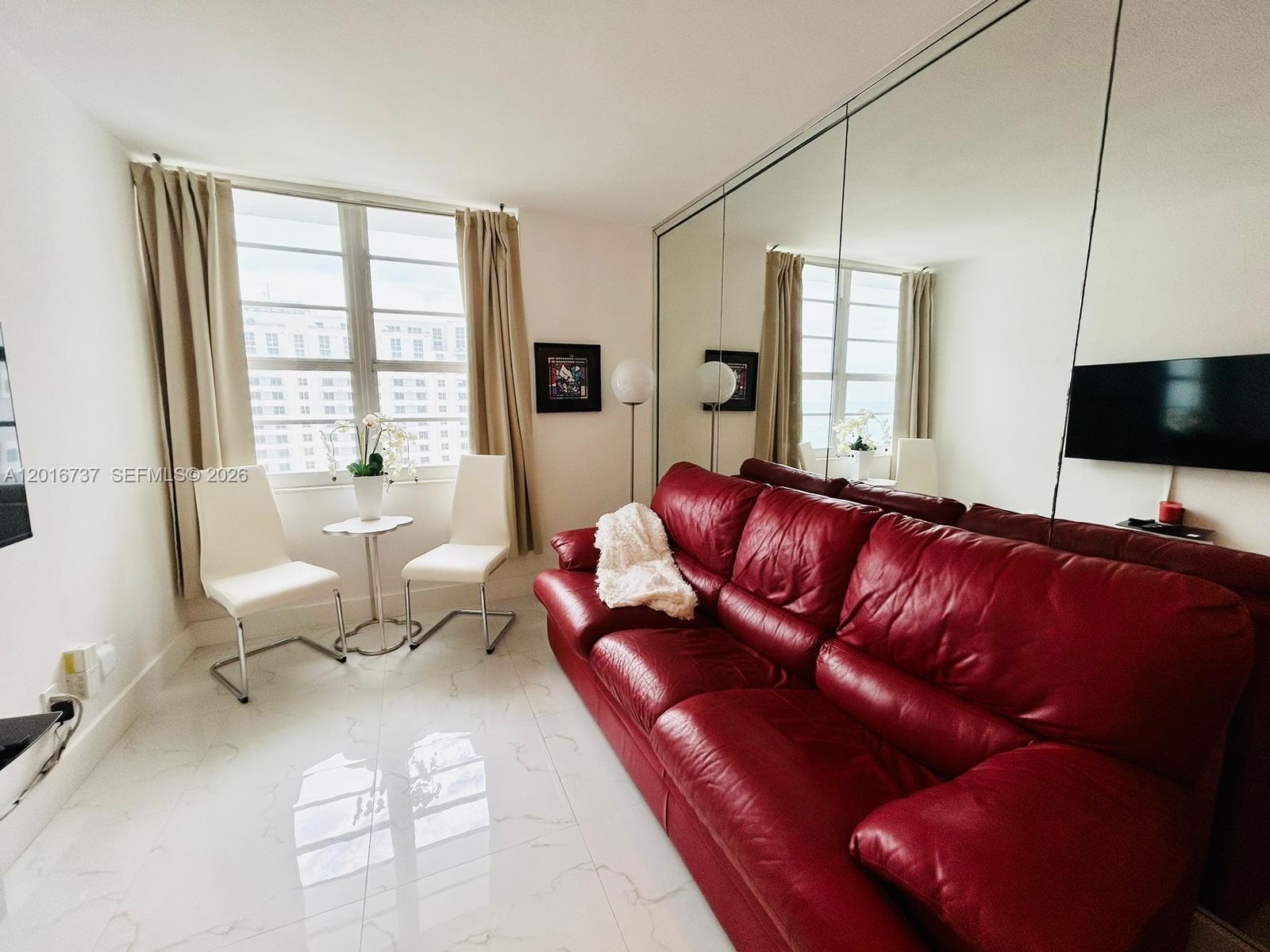 A living room features a red leather sofa, white chairs, a small table, and mirrored walls — 100 Lincoln Rd # 1526, Miami Beach FL 33139, MIAMI BEACH, FL